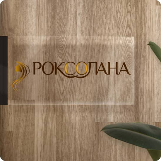 Прозора вивіска на фоні деревяної стіни з логотипом салону краси Роксолана