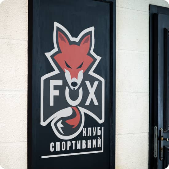 Фасад приміщення на якому видно непрозоре чорне вікно з великим логотипом: червона ілюстрація лисиці з надписом FOX спортивний клуб
